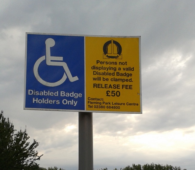 a disable parking sign: persons not displaying a valid disabled badge will be clamped. Is the English correct?