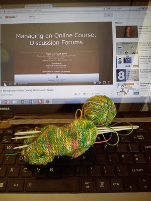 Computer showing video on online forums, with knitting on the keyboard