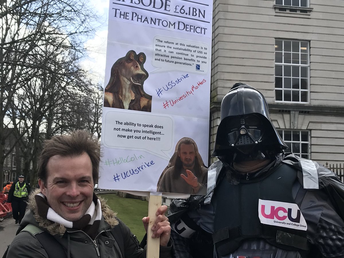Protestors at a rally, one dressed as Darth Vader, another holiding a sign about 'The Phantom Deficit'.