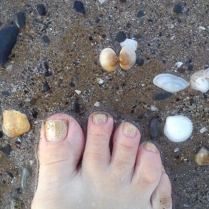 Bare foot with gold nail polish on sandy beach with shells