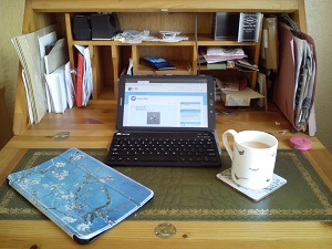Samsung Galaxy tablet set up in cover with keyboard, on a desk, with another cover (decorated with Japanese painting of cherry blossom) and a cup of tea.