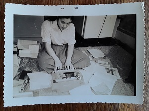 Young Japanese woman sitting on floor typing. Above the photo it says 'Jan 58'.