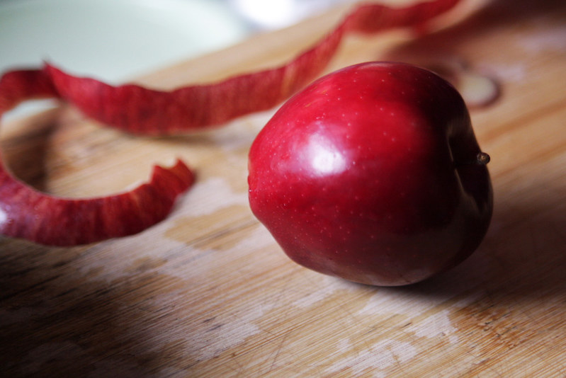 A red apple on a wooden chopping board with a strip of apple peel