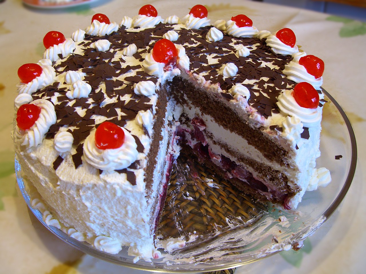 A chocolate cake with cherries and cream. One slice has been removed to reveal the layers of cake and cream inside