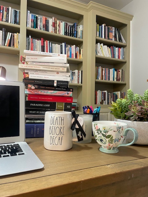 Desk with books, laptop, new floral cup, and mug with words 'Death Before Decaf' in black letters