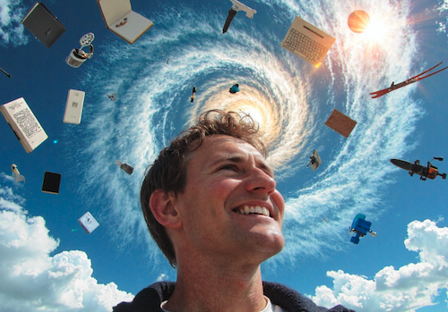 A photorealistic 4:3 format image of the author in his fifties, full head of mousy brown hair, cheeky grin, full of ideas looking up at a sky that is a vortex of visualised ideas: books, mirrors, a QWERTY keyboard, microphone, smartphone, MRI scan, skis, and words like: reflect, comment, share, collaborate, AI, motivation, communication, reading, learning.